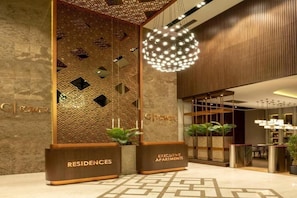 A modern hotel lobby with a reception desk, a decorative wall with geometric patterns, and a hanging spherical light fixture.