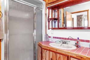 A bathroom with a wooden vanity, a sink, a mirror, and a shower door.