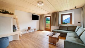 Een houten plafond, een flatscreen televisie, een bank, een bijzettafeltje en een raam met gordijnen.