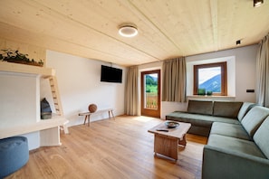 A wooden ceiling, a flat-screen TV, a sofa, a coffee table, and a window with curtains.