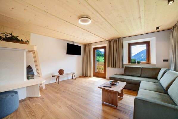 A wooden ceiling, a flat-screen TV, a sofa, a coffee table, and a window with curtains.