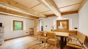 Een kamer met een houten plafond, een eettafel met stoelen, een bankje en een raam met uitzicht op groen.