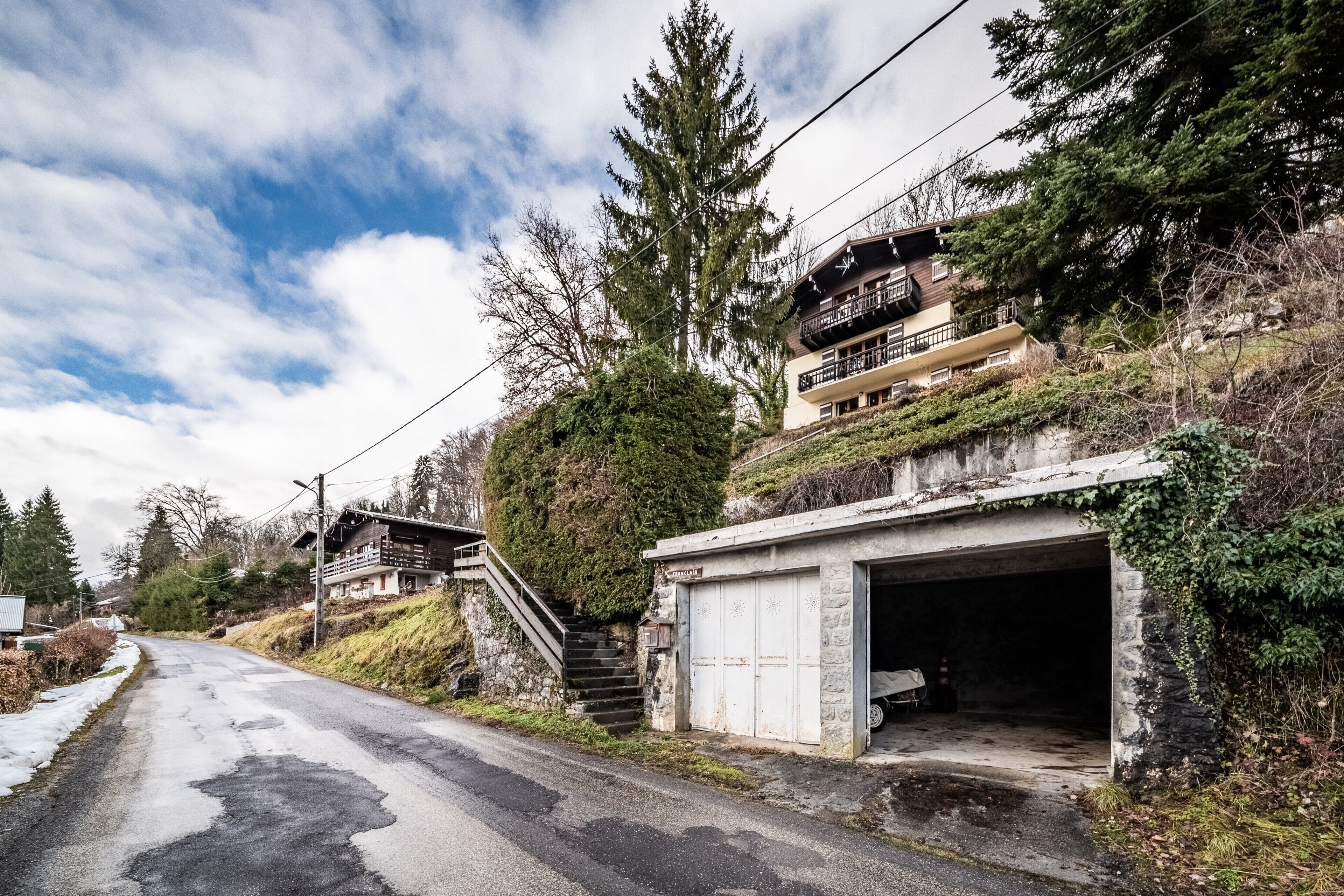 Une route de campagne avec un garage et un escalier menant à une maison.