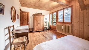 A wooden-paneled room with a bed, a wooden wardrobe, a table with a chair, and a window with a mountain view. - Chalet 'Franclair' with Mountain View, Shared Garden and Wi-Fi (Samoëns)