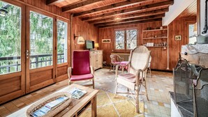 A wooden interior with a dining area, a red chair, wicker furniture, and a fireplace. - Chalet 'Franclair' with Mountain View, Shared Garden and Wi-Fi (Samoëns)