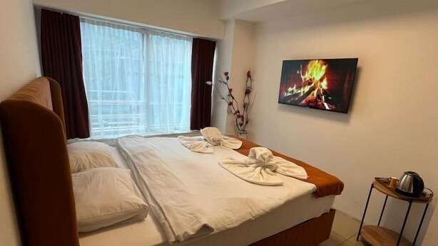 A neatly made bed with white linens and towels, a small bedside table with a kettle, and a painting of a fire on the wall. - Kadıköy Bull Hotel (Istanbul)