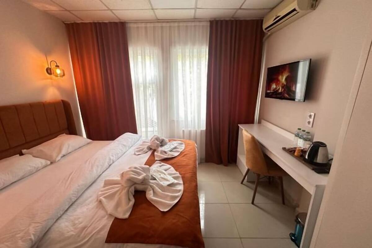 Hotellihuone, jossa on sänky, työpöytä, televisio ja ikkuna, jossa on verhot.