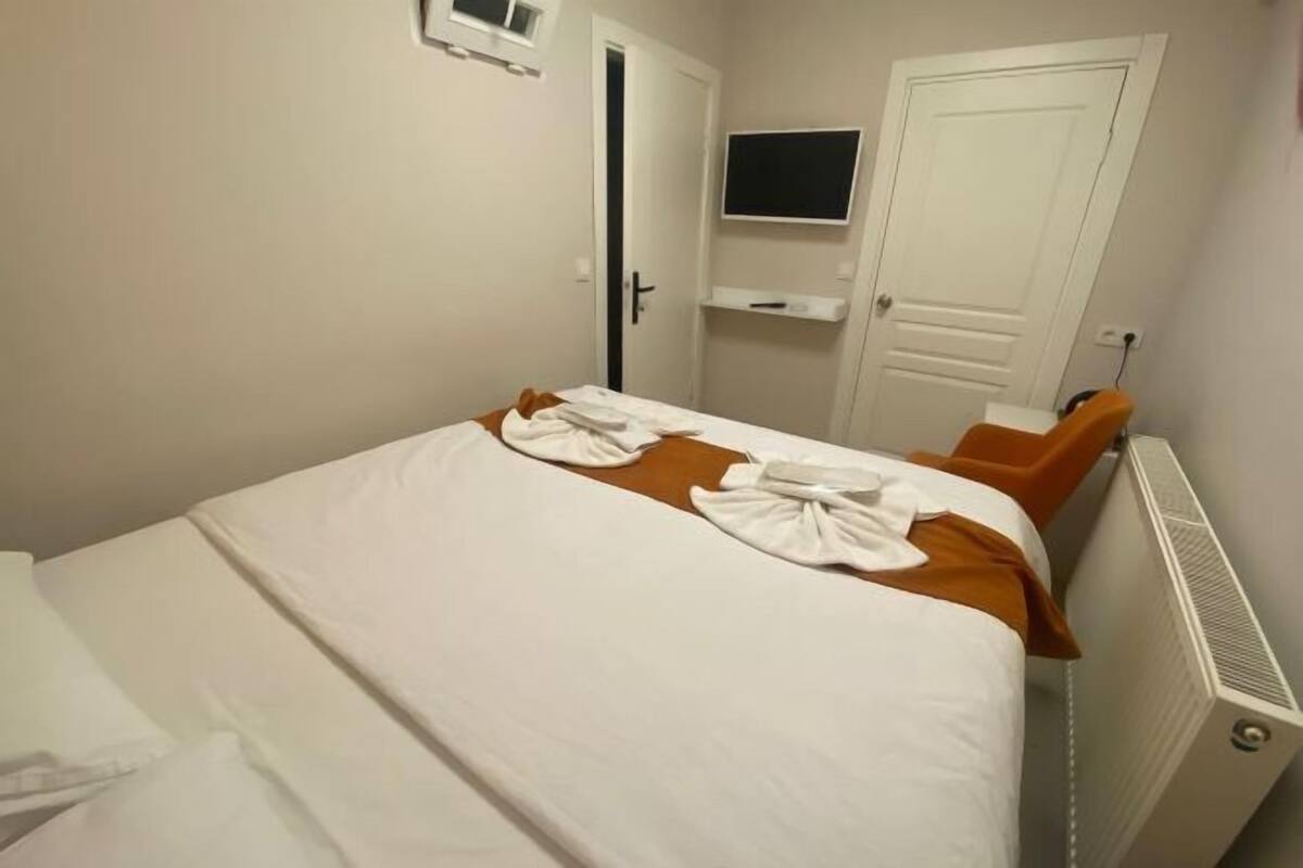 Hotellihuone, jossa on sänky, seinälle asennettu televisio ja patteri.