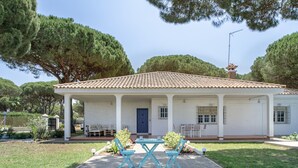 Un bâtiment d’un seul étage, doté d’un toit recouvert de tuiles, d’un porche avec des sièges extérieurs et d’une porte bleue.