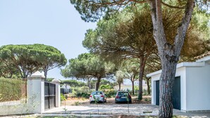 Une rue résidentielle où sont garées deux voitures, avec des arbres et un bâtiment blanc doté d’un garage.