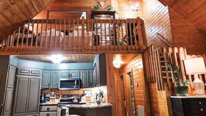 A rustic cabin interior with a kitchen, dining area, and a loft bedroom.