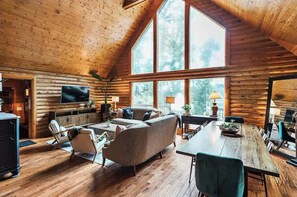A log cabin interior with a large dining table, a sofa, and a TV mounted on the wall. - Lakefront log cabin (Eastover)