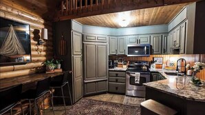 A compact kitchen with grey cabinets, a central island with bar stools, a hanging light fixture, and a wooden ceiling.