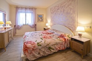 Una camera da letto con un letto, comodini, una cassettiera, una finestra con tende e un quadro appeso al muro.