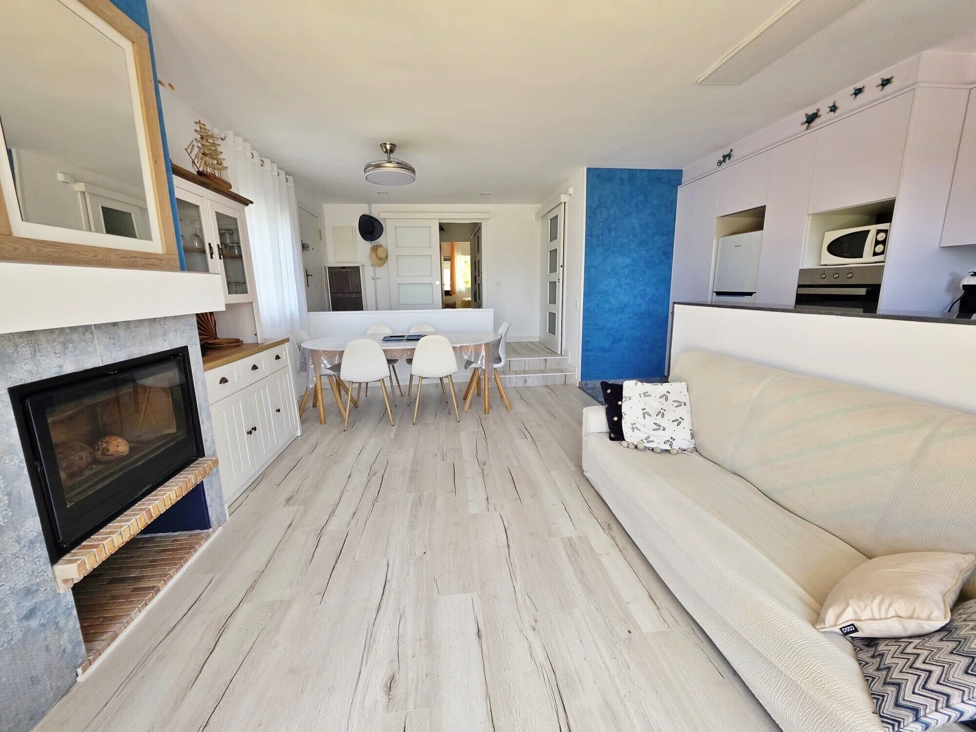 Ein modernes Wohnzimmer mit Kamin, einem Essbereich mit Tisch und Stühlen sowie einer Küche mit Schränken und Geräten.