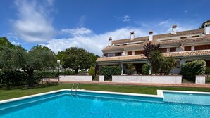 A swimming pool with a clear blue water, surrounded by a well-maintained lawn and a large building with a tiled roof in the background. - Apartment 'Fantástico S´agaró' with Shared Pool, Private Terrace and Shared Garden (S'Agaró)