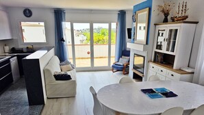 A modern kitchen with a dining area, a sofa, a chair, a table, and a view through the glass door. - Apartment 'Fantástico S´agaró' with Shared Pool, Private Terrace and Shared Garden (S'Agaró)