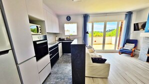 A modern kitchen with a dining area, a sofa, and a view of greenery. - Apartment 'Fantástico S´agaró' with Shared Pool, Private Terrace and Shared Garden (S'Agaró)