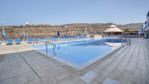 A swimming pool with lounge chairs and a gazebo, surrounded by a rocky landscape. - Taurito's Sea Sunset View: Sea Views, Shared Pool & Wi-Fi (Taurito)
