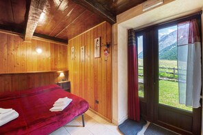A wooden room with a bed, a nightstand, a door leading to a balcony with a mountain view. - Room '3' with Mountain View, Shared Terrace and Wi-Fi (Rhêmes-Notre-Dame)