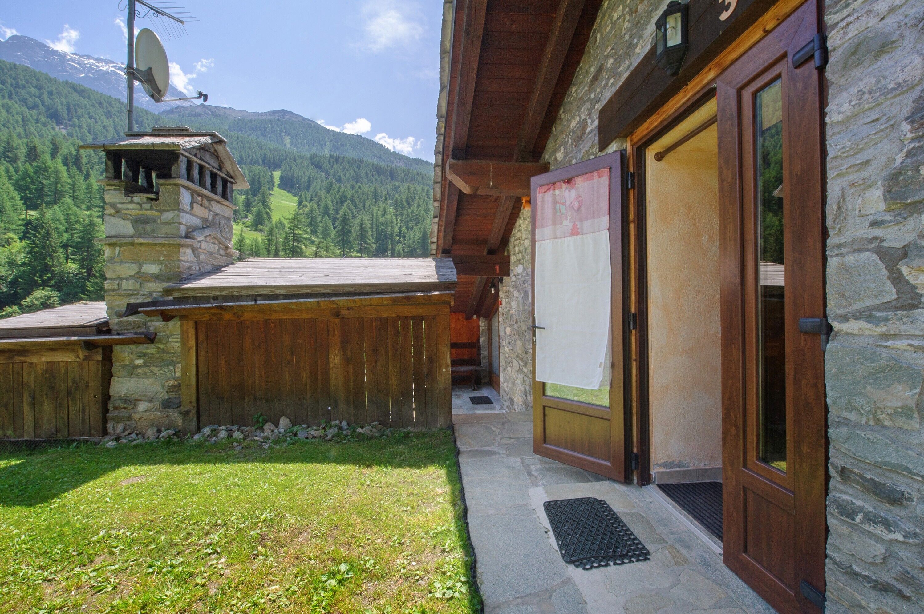 A stone building with a wooden door, a satellite dish, and a view of mountains.