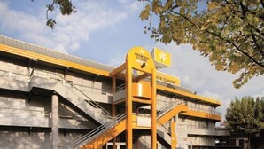 Ein modernes Gebäude mit gelbem Eingangsschild, mehreren Treppen und einem Parkplatz.