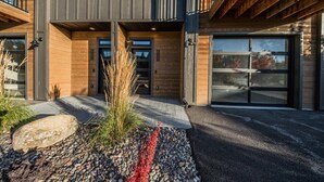 A modern two-story house with a garage, large windows, and a stone pathway leading to the entrance. - New 3BR/3BA Condo Steps from Flathead Lake (Lakeside)