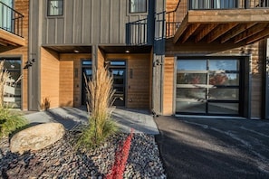 A modern two-story house with a garage, large windows, and a stone pathway leading to the entrance. - New 3BR/3BA Condo Steps from Flathead Lake (Lakeside)