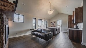 A spacious living area with a sofa, a kitchen with wooden cabinets, and a dining area. - New 3BR/3BA Condo Steps from Flathead Lake (Lakeside)