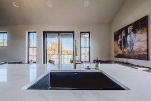 A spacious room with a large white marble sink, a painting on the wall, and a view through the windows. - New 3BR/3BA Condo Steps from Flathead Lake (Lakeside)