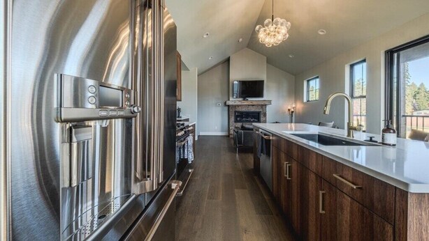 A modern kitchen with stainless steel appliances, a large island, and a view of the outdoors. - New 3BR/3BA Condo Steps from Flathead Lake (Lakeside)