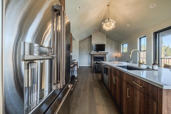 A modern kitchen with stainless steel appliances, a large island, and a view of the outdoors. - New 3BR/3BA Condo Steps from Flathead Lake (Lakeside)