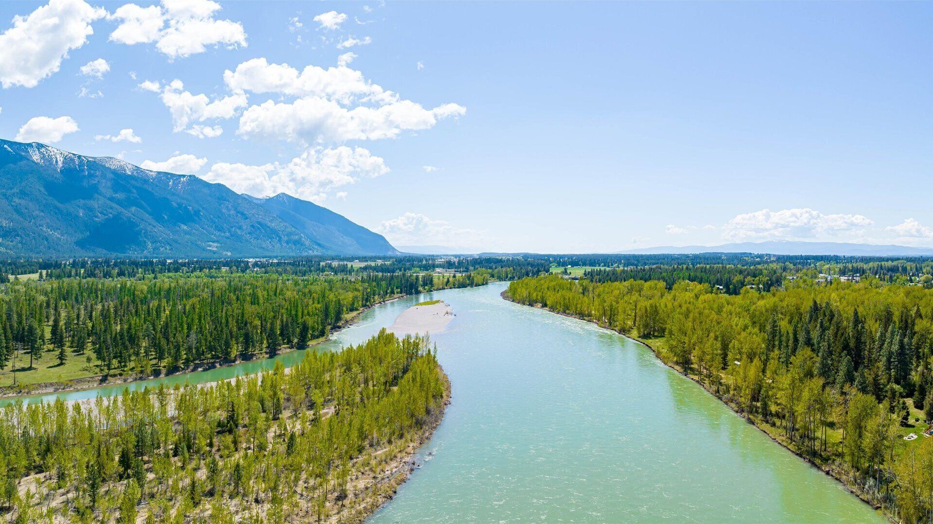 Une rivière serpentant à travers une vallée boisée, avec des montagnes en arrière-plan.