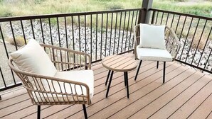 Eine Holzterrasse mit zwei Korbstühlen und einem kleinen runden Tisch.
