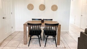 Ein Essbereich mit einem Holztisch, schwarzen Stühlen, einer gewebten Wanddekoration und einer sechseckigen Deckenleuchte.