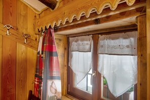 A wooden cabin interior with a window, a door with a white curtain, and a red plaid curtain hanging on a hook.