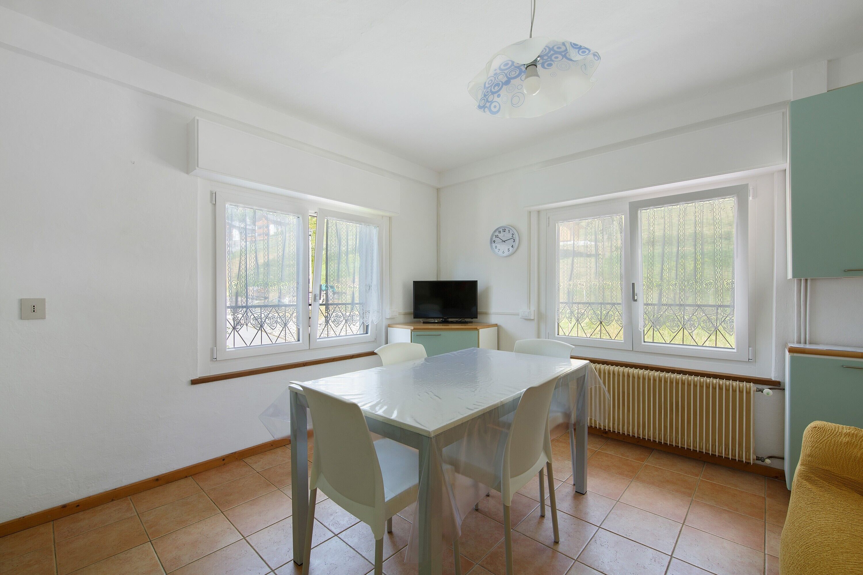 A room with a dining table, chairs, a television, and large windows.