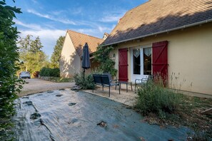 A house with a covered patio, a car parked in the driveway, and a red shutter on the window.