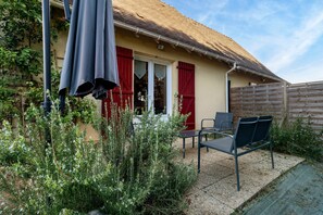 A patio with a table and chairs, a covered area with a table and chairs, and a building with a red shutter and a tiled roof.