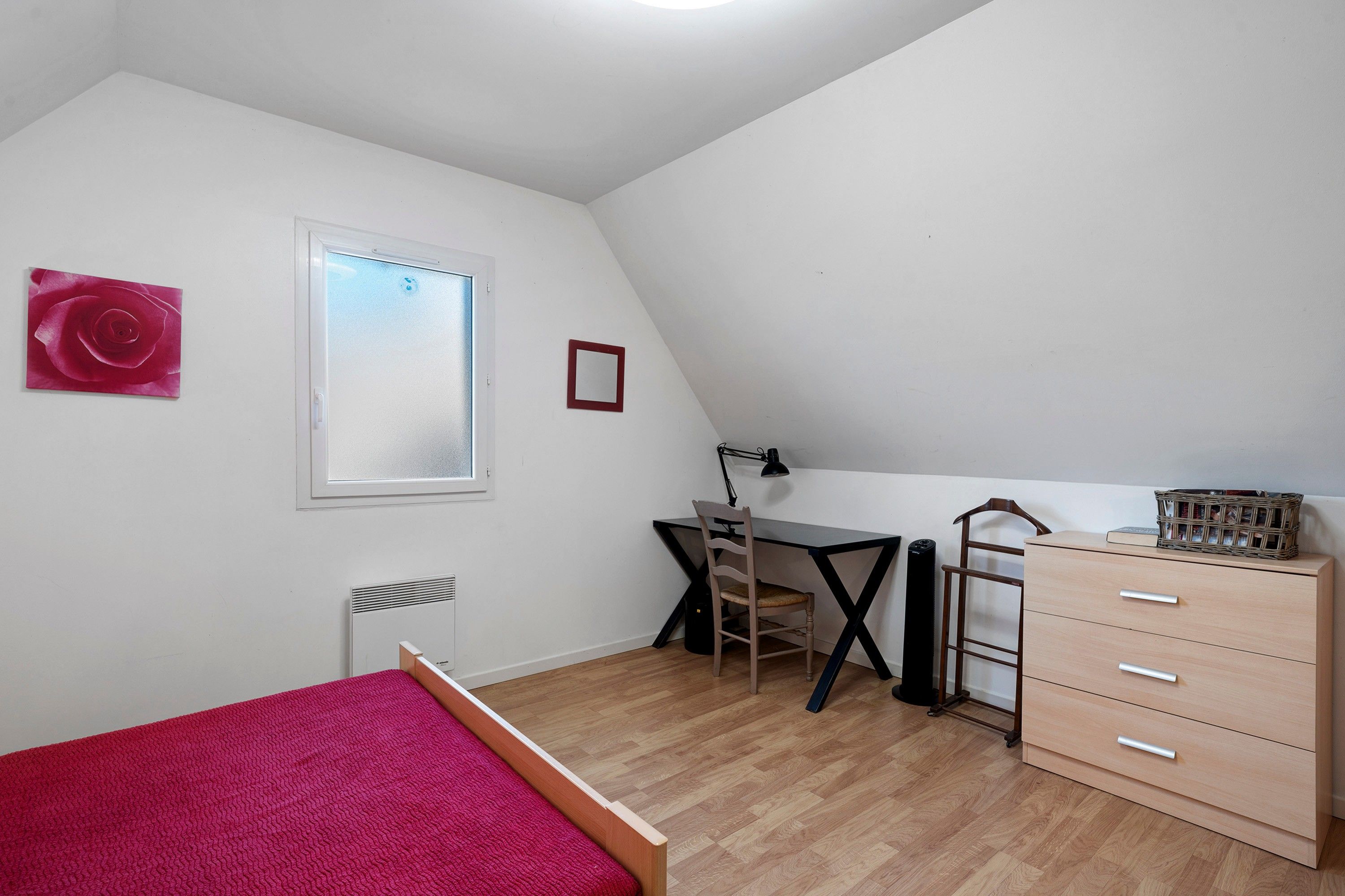 A bedroom with a bed, a desk, a chair, a dresser, and a radiator.