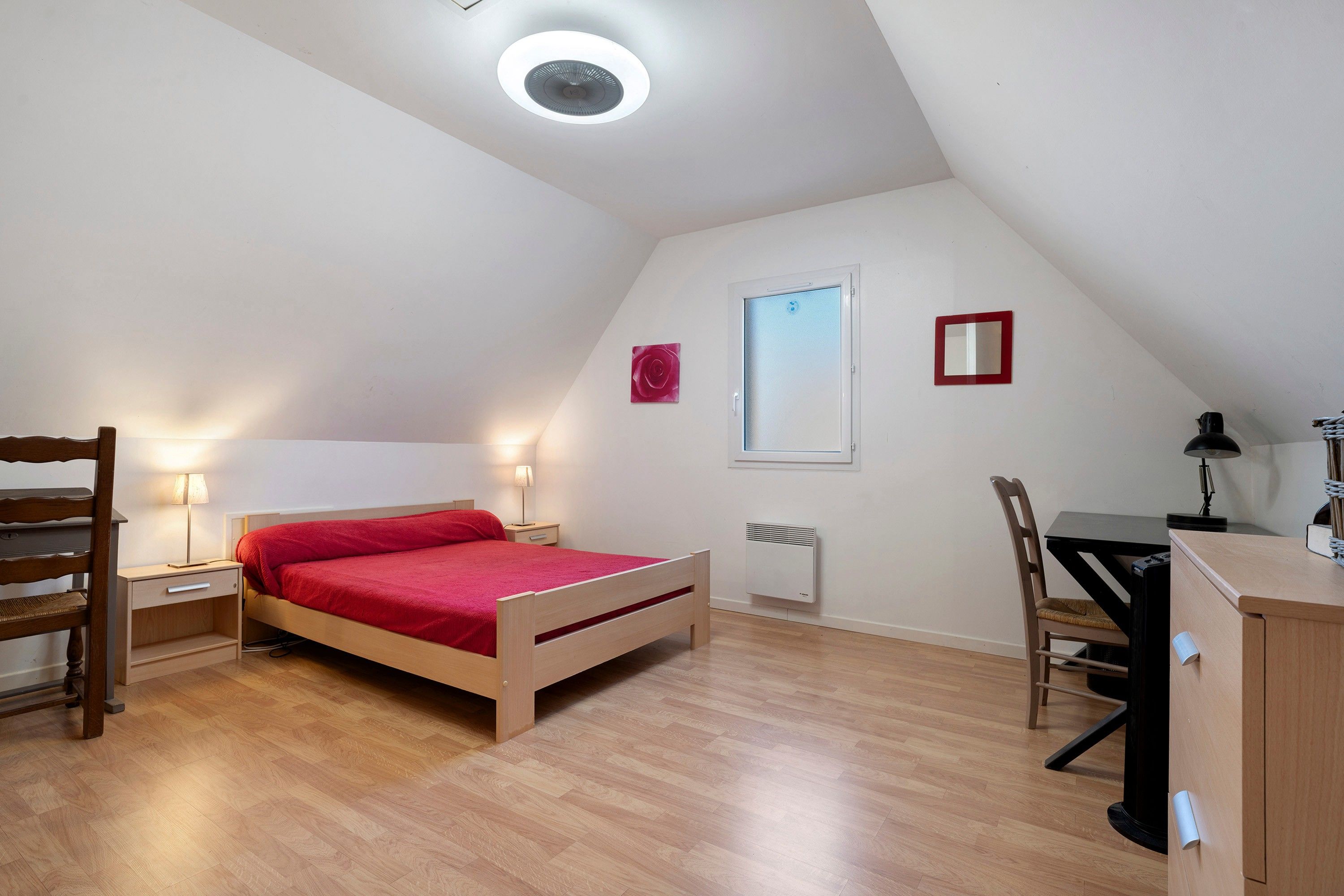 Une petite pièce bien éclairée, avec un lit, des tables de chevet, un bureau et une chaise.