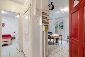 A room with a bed, a dining table with chairs, a red door, and a wall-mounted clock.
