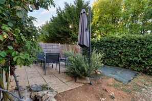 A patio area with a table and chairs, surrounded by a wooden fence and dense foliage. - Maison Montagnac – Peaceful Retreat with Garden in the Heart of the Lot (gignac)