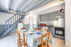 Uma sala de jantar com uma mesa posta para quatro pessoas, uma escadaria e uma cozinha equipada com eletrodomésticos modernos.