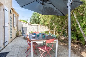 Um pátio externo com uma mesa, cadeiras e um guarda-sol.