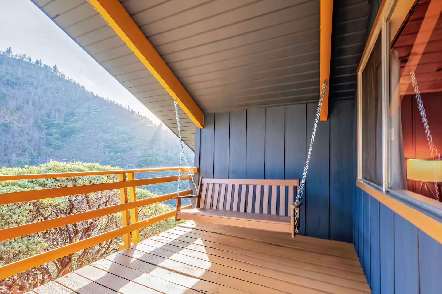 A wooden deck with a swing chair, a railing, and a view of a forested hillside.