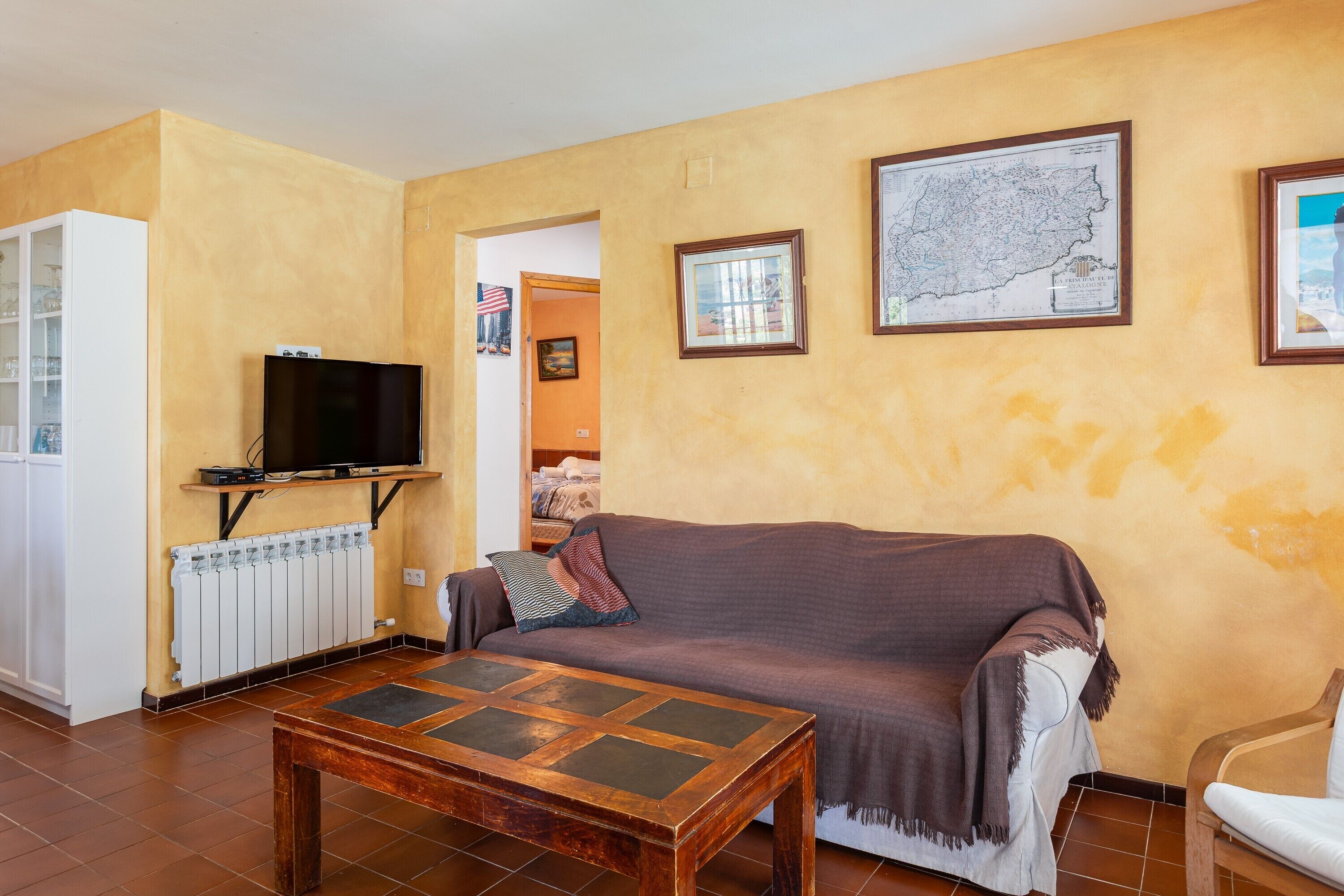 A living room with a sofa, a coffee table, a television, and a map on the wall.
