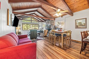 Amplia sala de estar con un sofá rojo, una mesa de comedor de madera y sillas, una chimenea y un ventilador de techo.