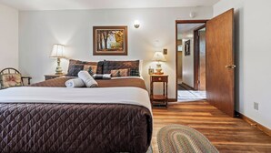 A bedroom with a bed, two bedside tables with lamps, a painting on the wall, and a wooden door. - Cedar Pine Cottage | Relaxing Cozy 2BR Cabin (Springville)