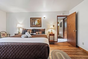 Une chambre à coucher avec un lit, deux tables de chevet avec des lampes, un tableau au mur et une porte en bois.